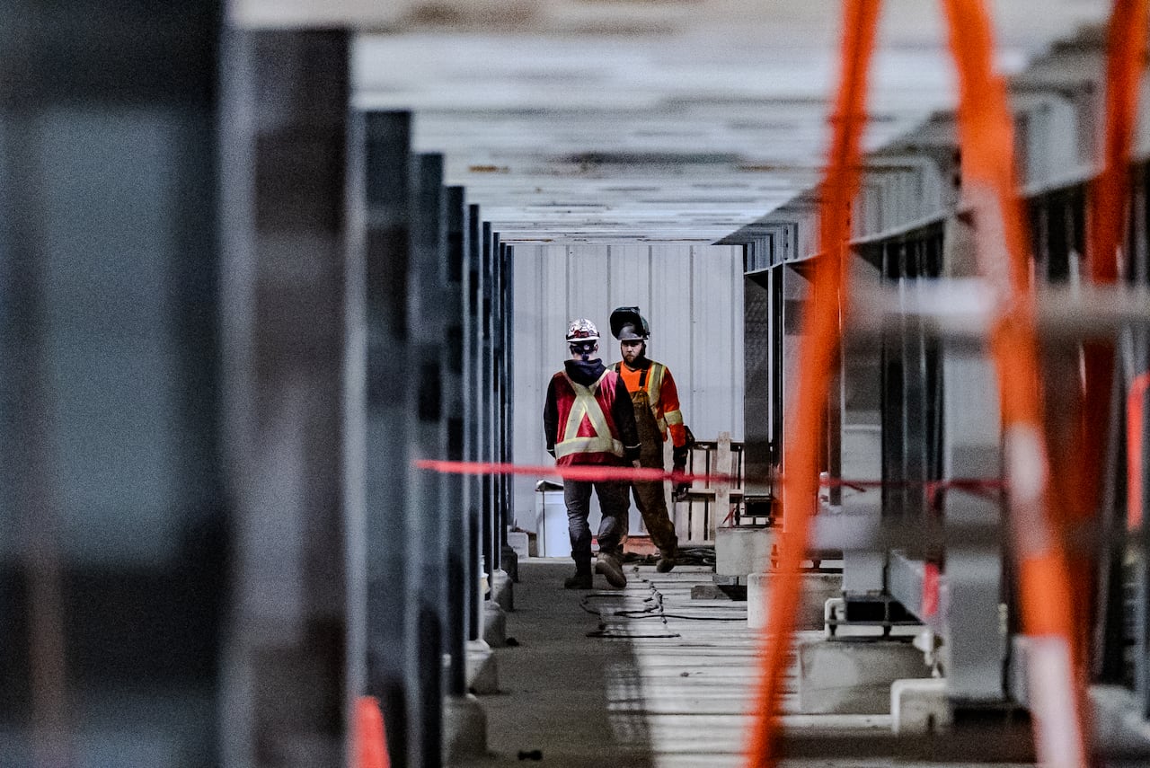 Two construction workers wearing yellow vests talking to each other inside a large building.