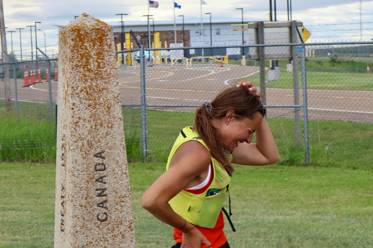 Woman in running gear next to a stone marker that reads Canada