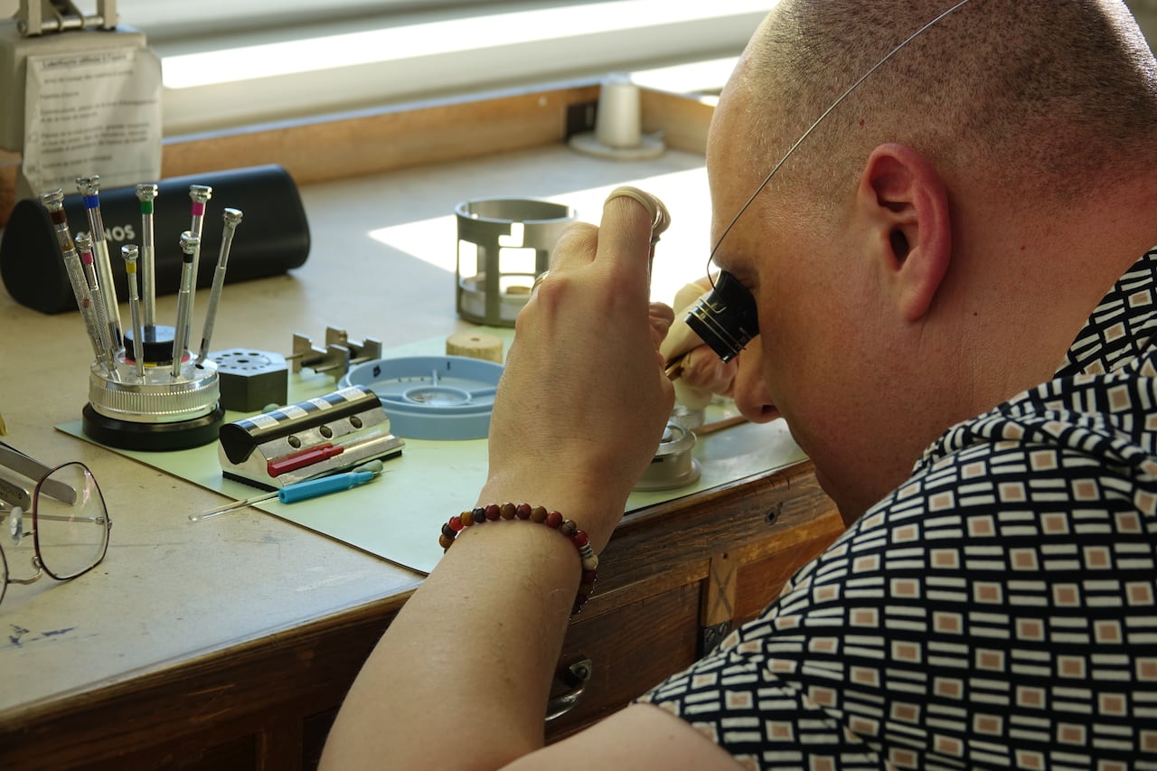 A man looking through a magnifying glass at small pieces.