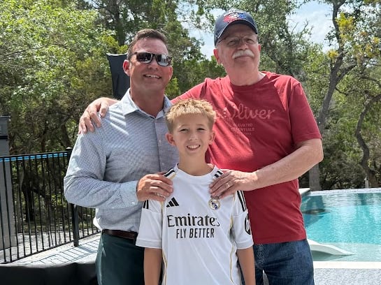 A group photo showing a boy, his father and grandfather with arms around each other in front of a pool.