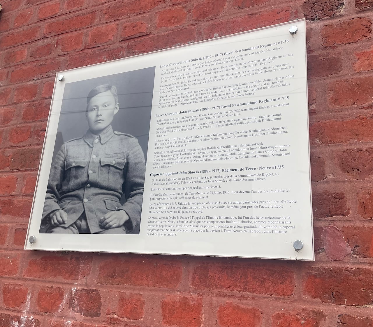 A plague commemorating Inuk war hero John Shiwak is posted in a brick wall.