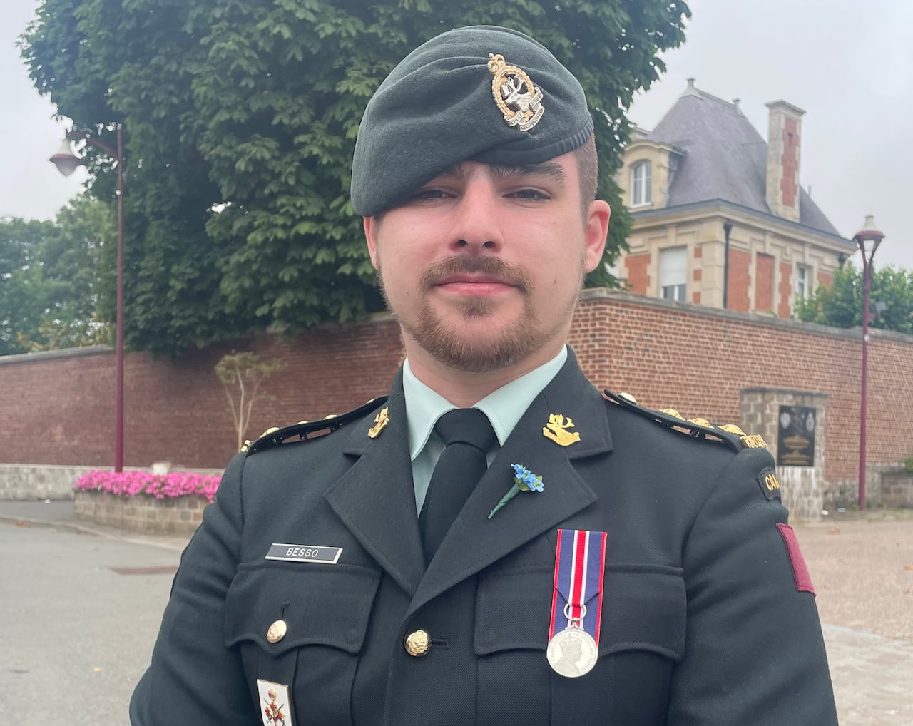 A man in a green military uniform stands outside.