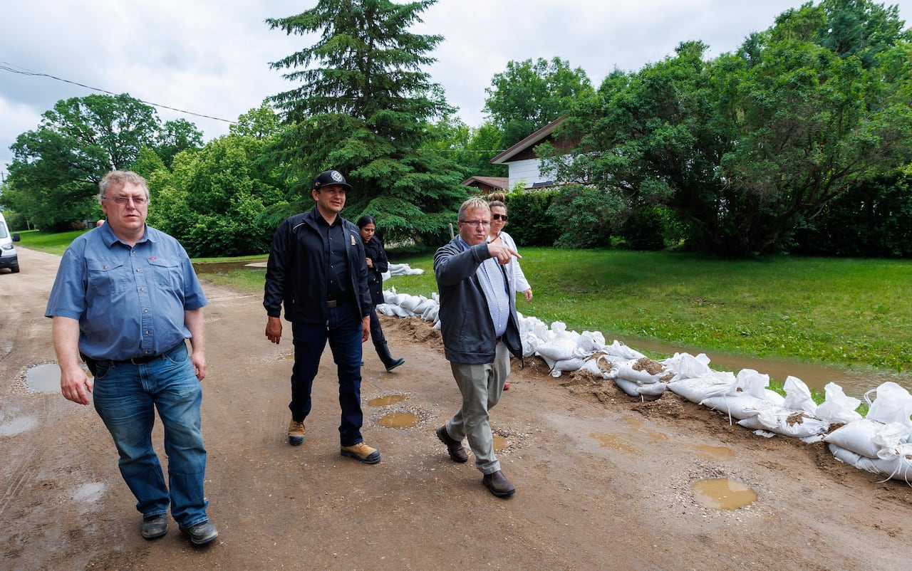 Three men walk along a dirt road with sandbags lined up on one side.