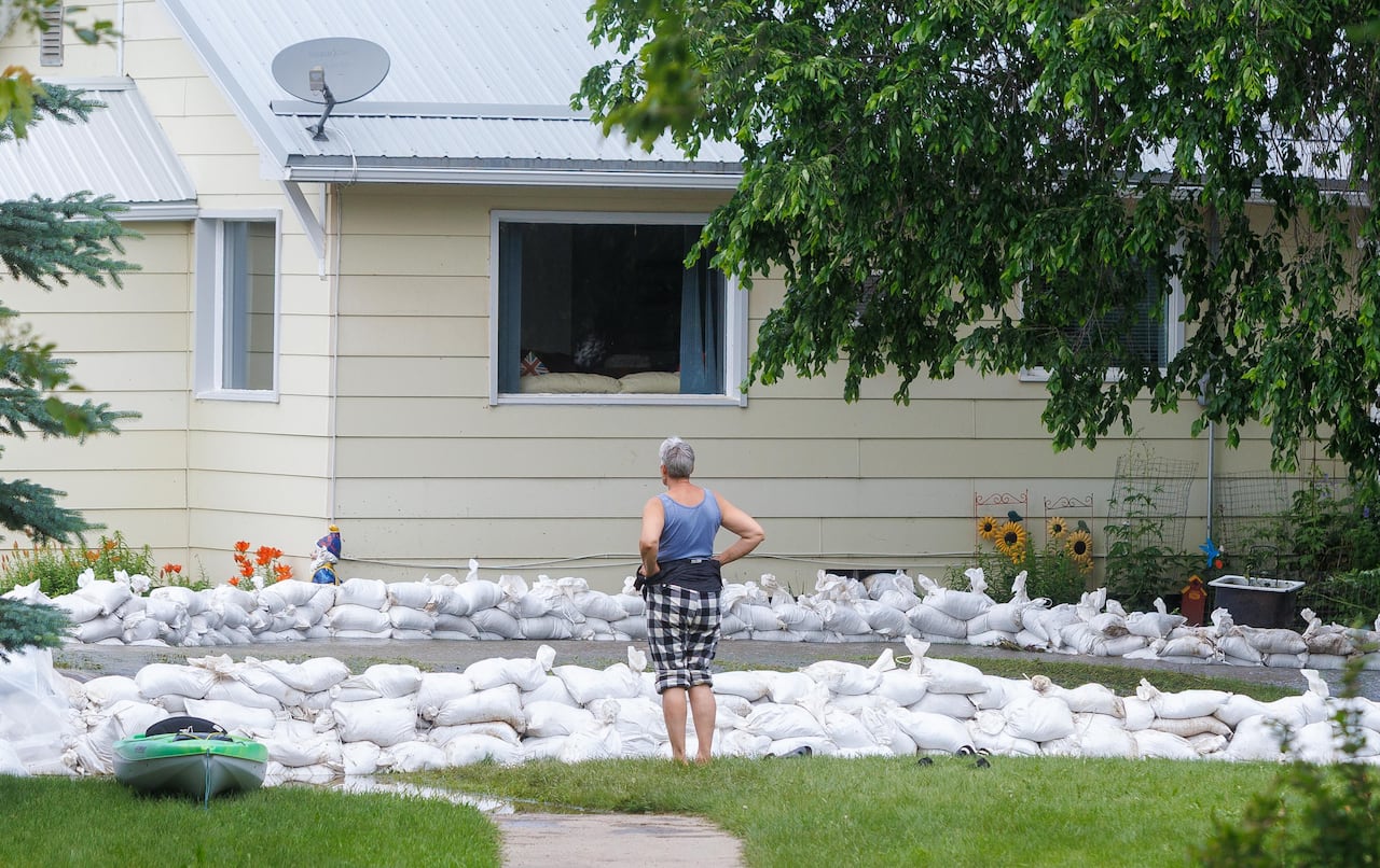 A person stands with hands on her hips as she looks at rows of sandbags in front of a house.