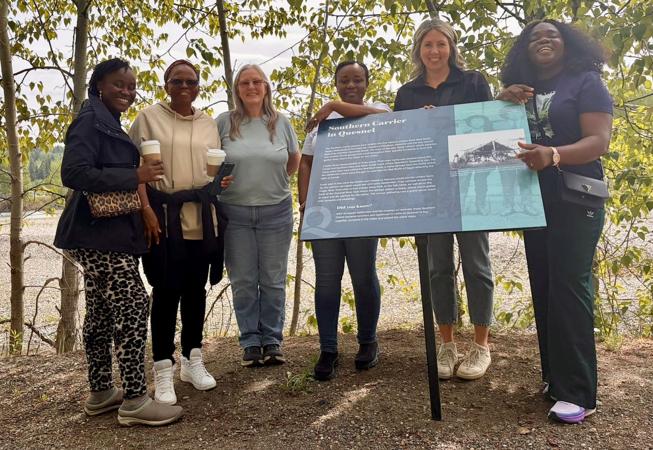 A group of women smile next to a sign on a forested trail.