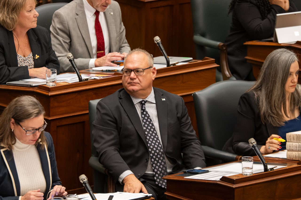 A man sitting at desk in the legislature looks to his side.