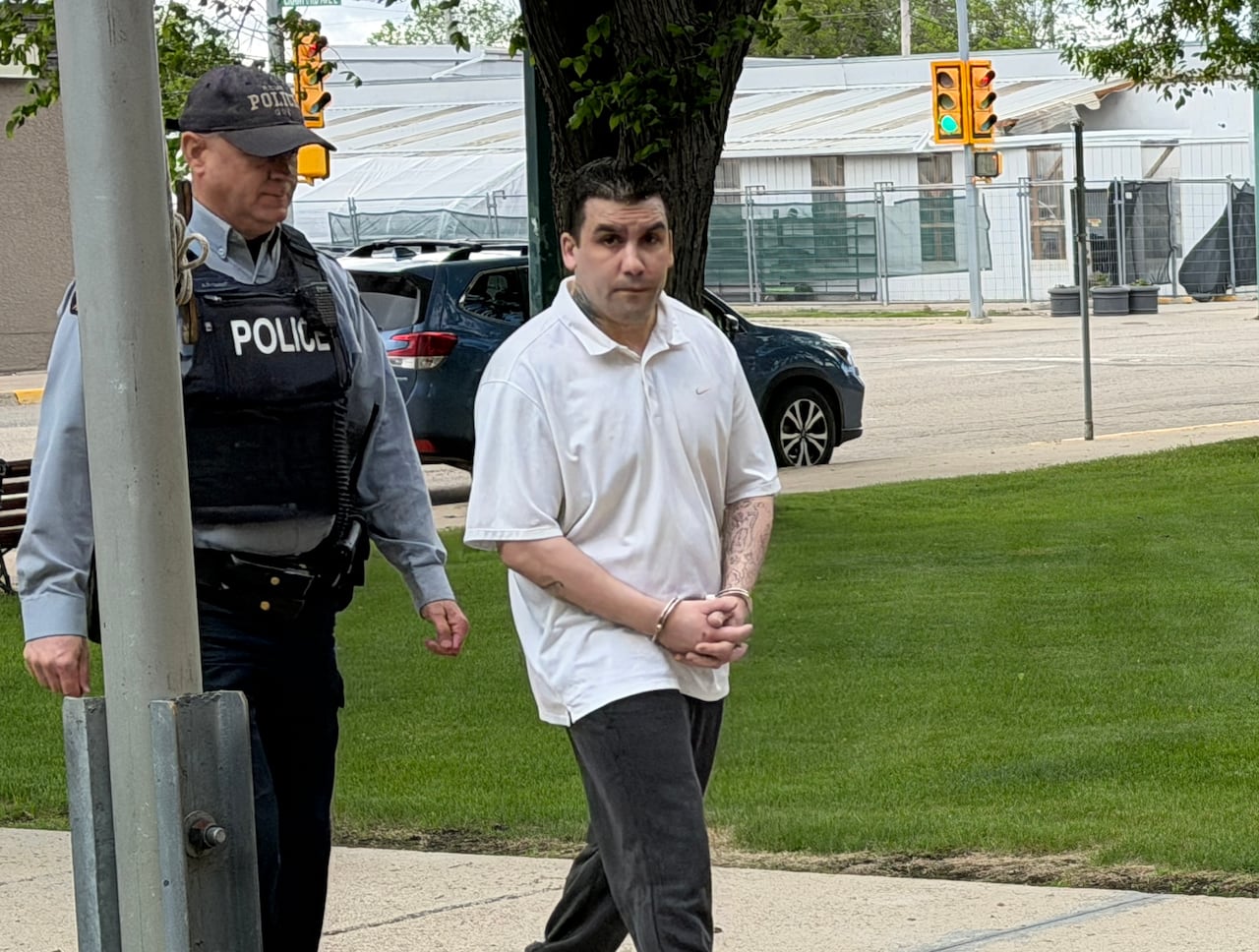 A man walks in handcuffs. He has a white shirt on.