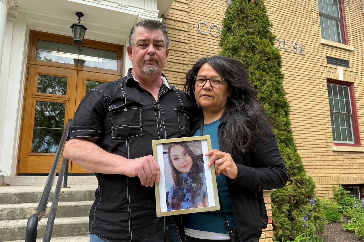 A man and a woman hold a photo of a young woman.