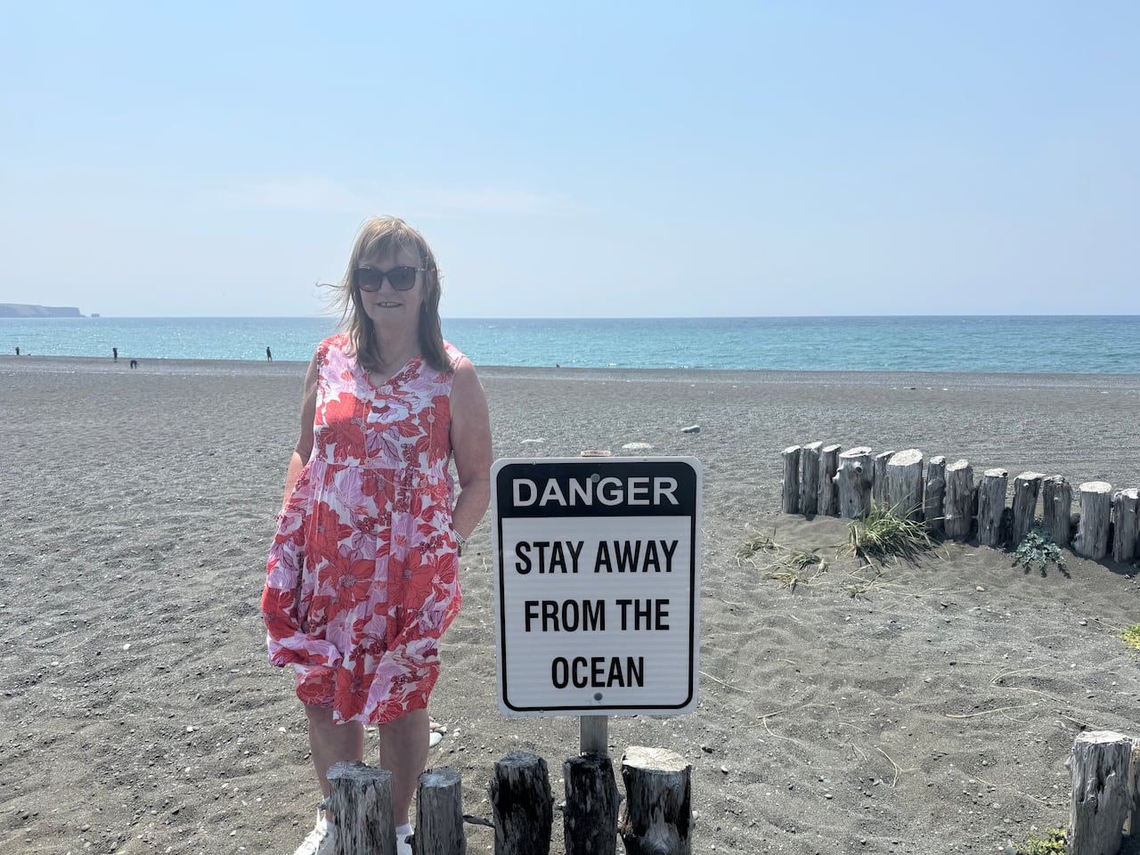 Verna Hayward, Mayor of St. Vincent's, standing by a sign on the beach that says "DANGER STAY AWAY FROM THE OCEAN."