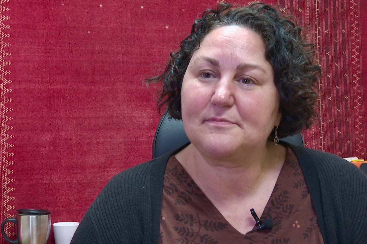 A person with short, black curly hair sits in front of a red, textured background.