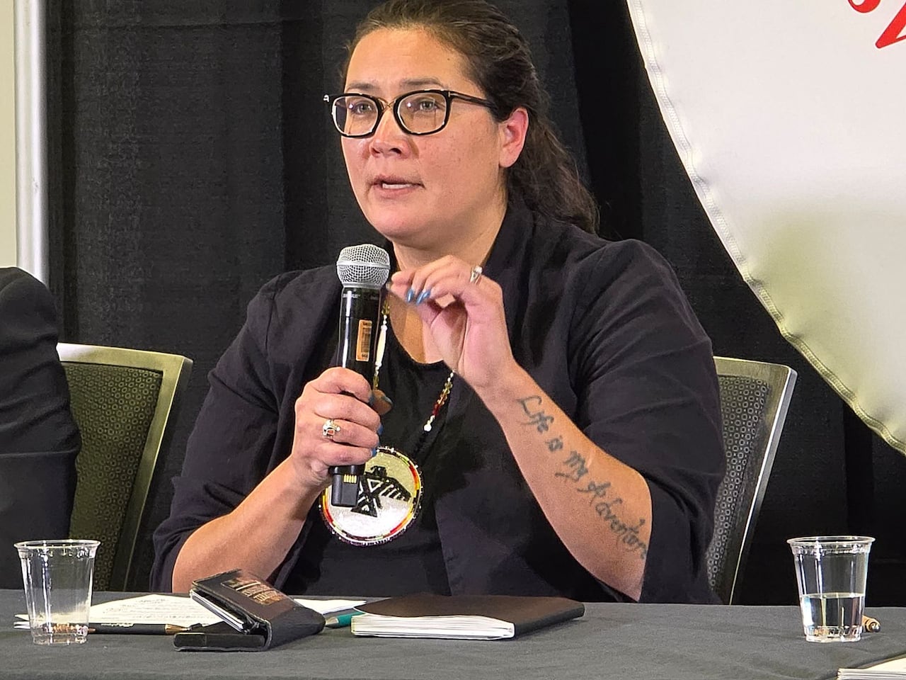 A woman with her long hair pulled back, wearing glasses, holds a microphone