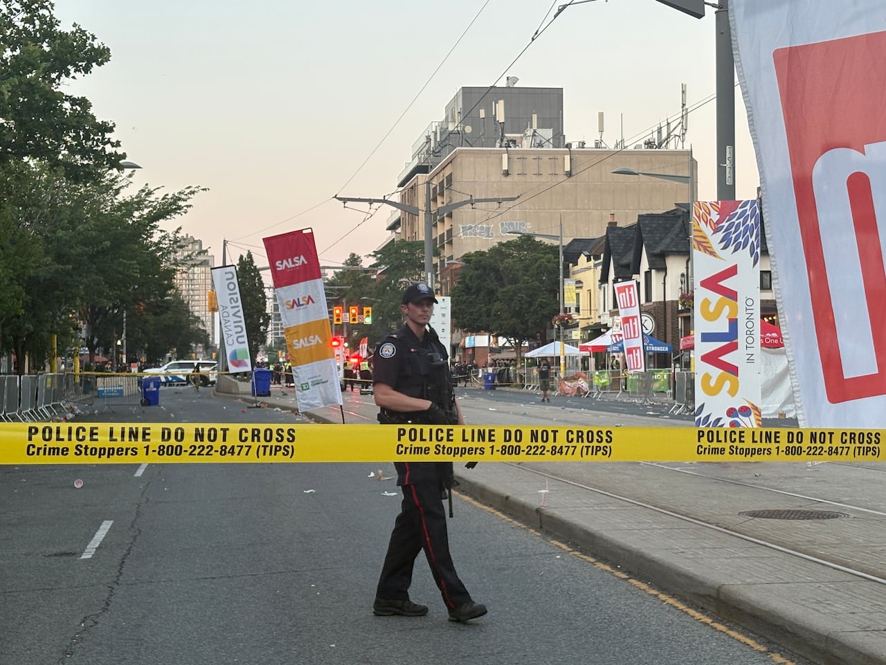 Police officer with gun at taped off area with salsa festival signage in the background.