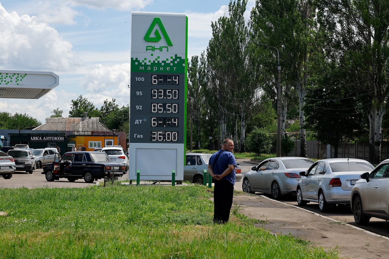 a man looks at a line of cars queuing to get into a gas station
