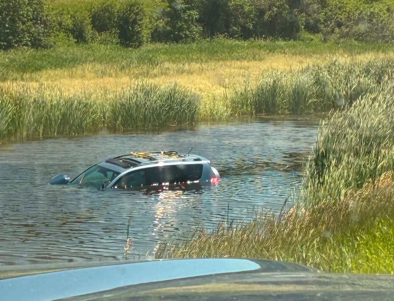An SUV sinking in a large pond, with only the roof and the tops of the window visible.