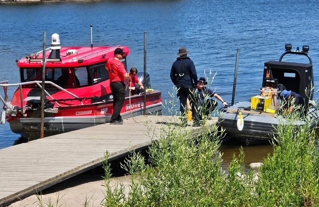 Two boats are seen at the end of a wooden dock on a lake.