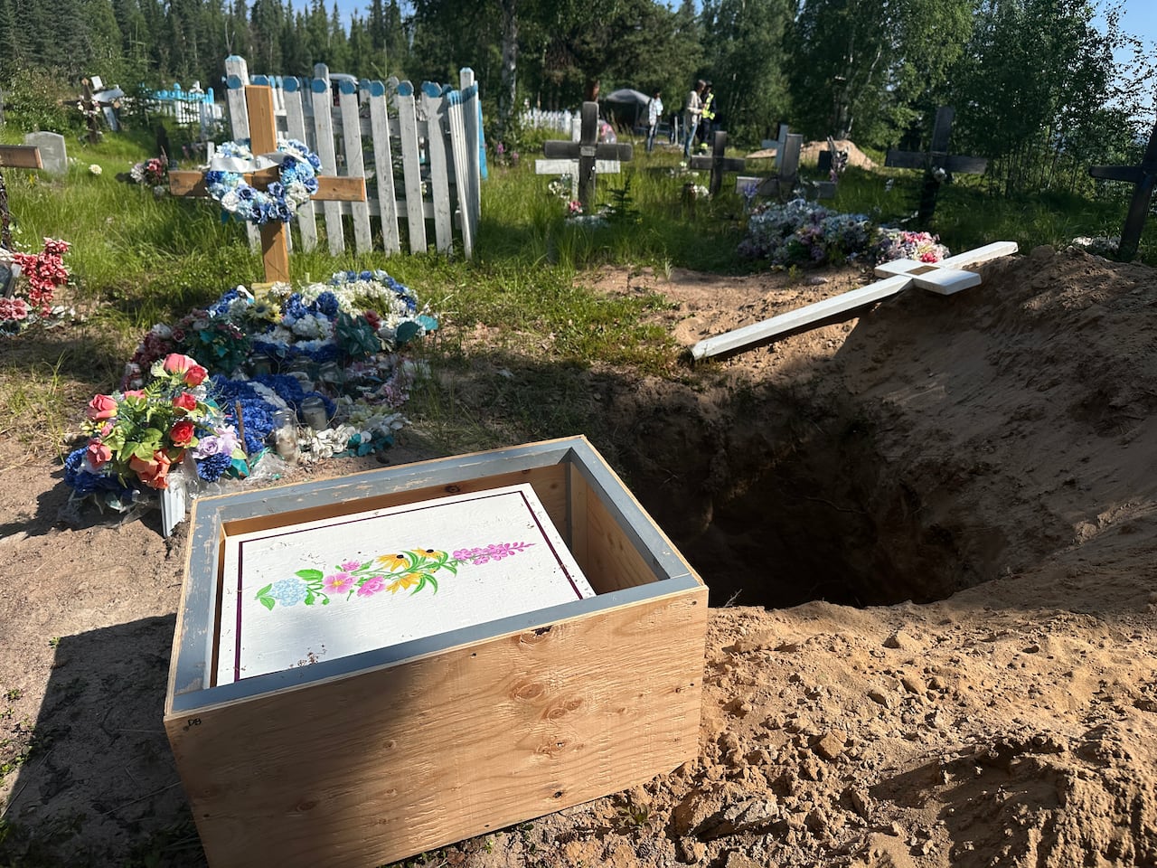 A small casket next to a hole in a grassy cemetery.