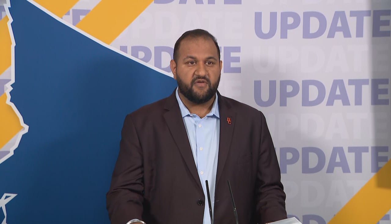 A bearded man in a blue dress shirt and blazer stands at a podium in front of a sign that says 'update.'