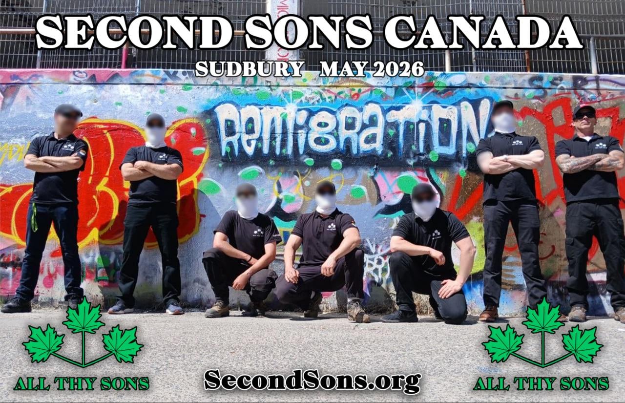 People pose with their arms crossed in all black. They stand in front of a parking garage covered in graffiti which says 'reimig
