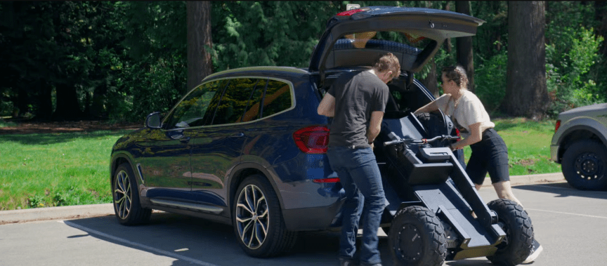 two people loading the folded UPT chassis into a BMW SUV