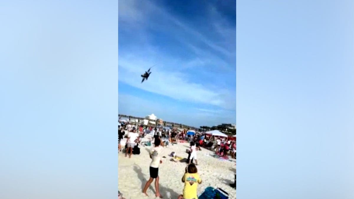 Blue Angels jet makes a low pass over Pensacola Beach as beachgoers cheer.
