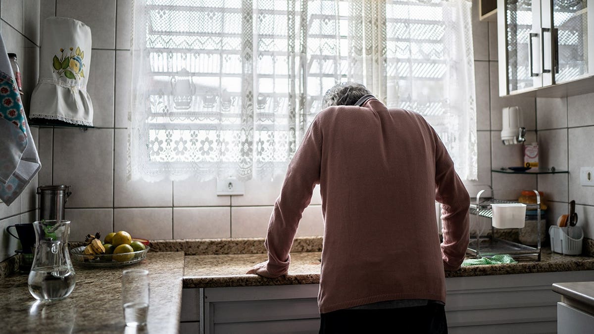 Senior man leans on counter while standing at home.