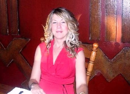 A woman with long hair sits at a kitchen table.