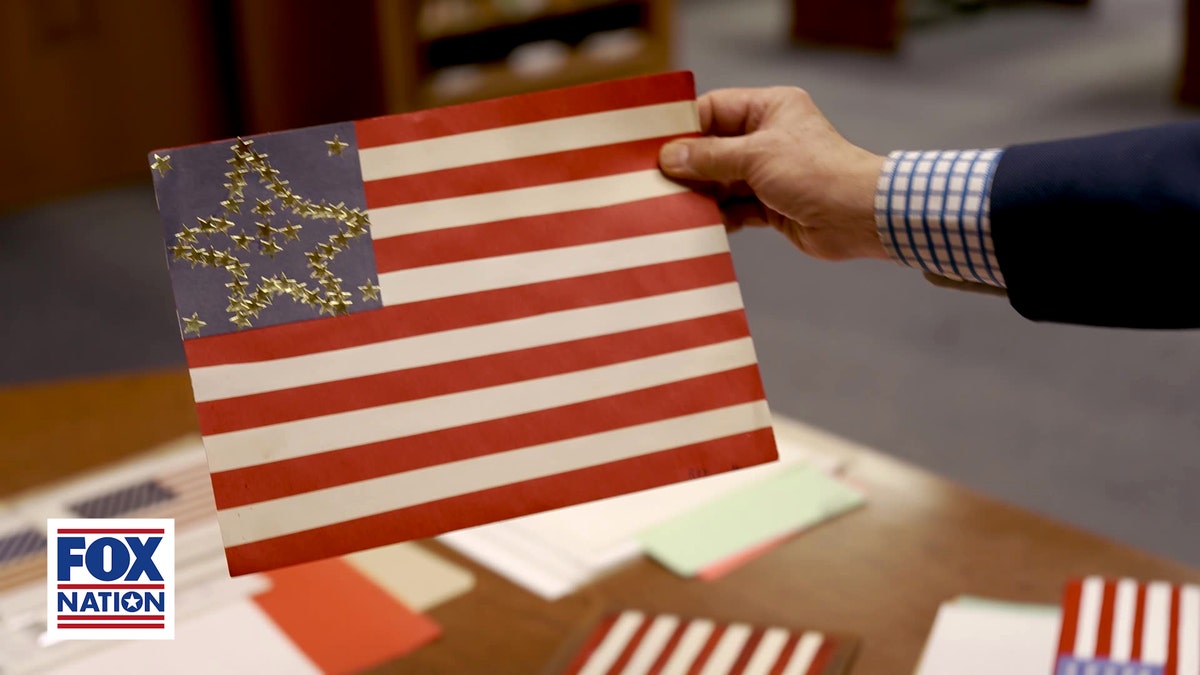 A hand holds a proposed 50-star U.S. flag design with the stars arranged in the shape of a large five-point star inside the blue canton.