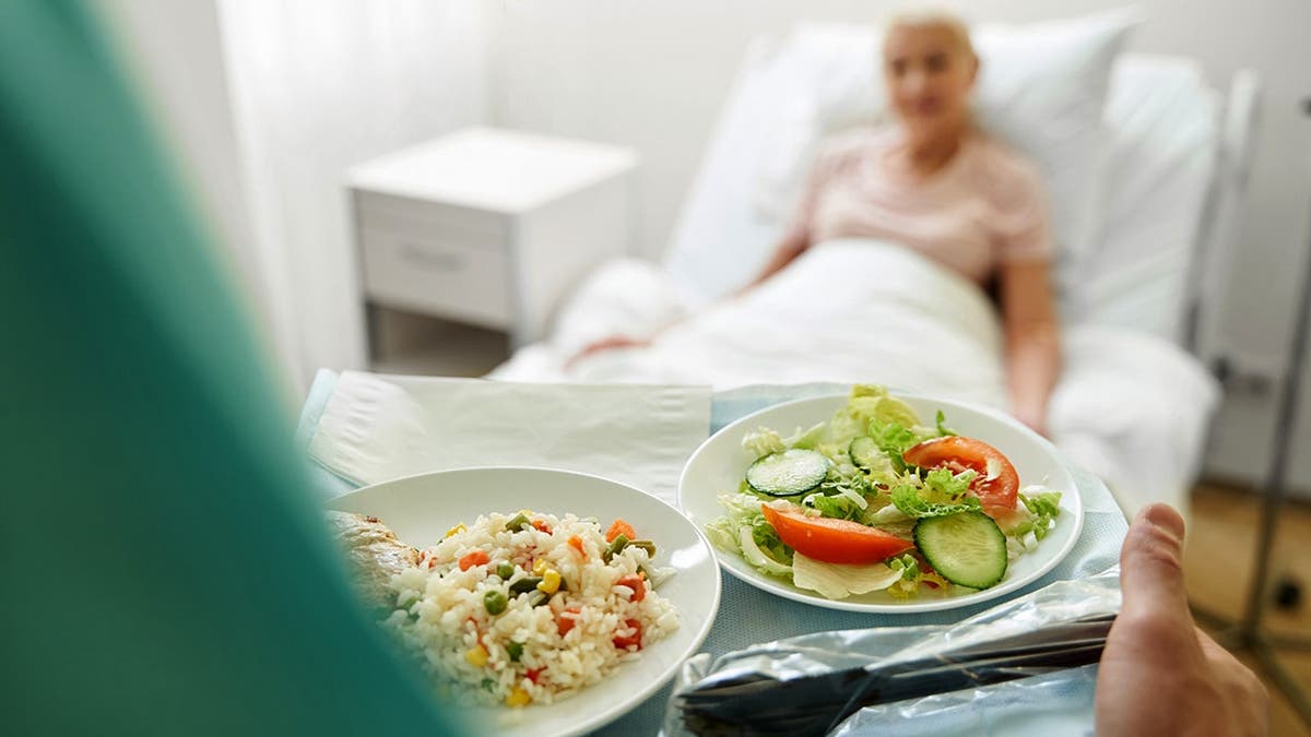 A nurse serves a patient a tray of food in a hospital.