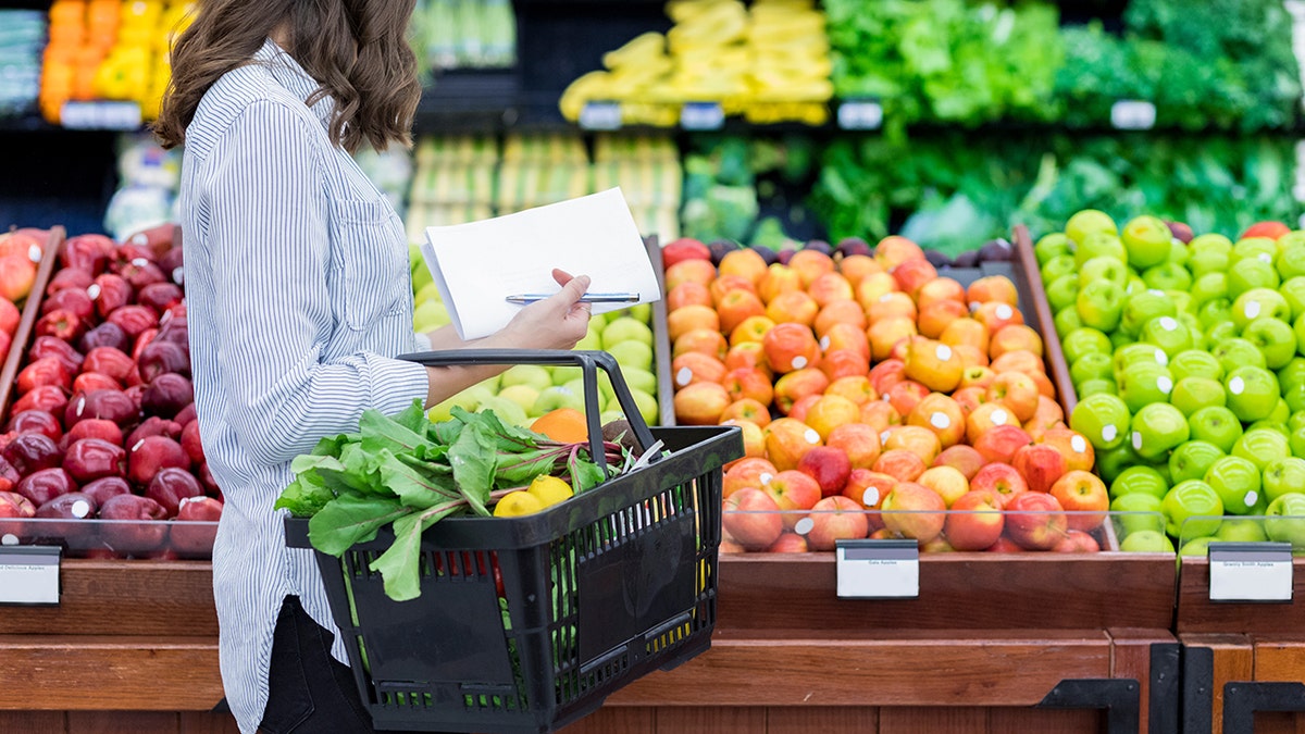 Woman shopping for fruit with grocery list.