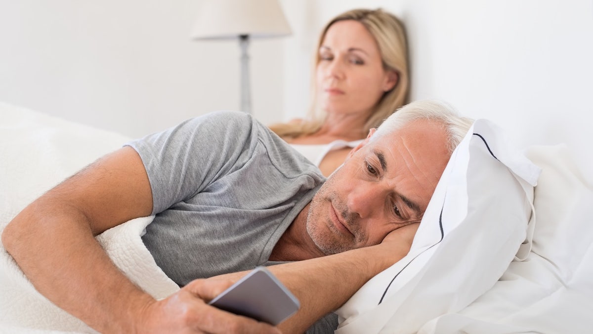 Man on phone in bed with wife