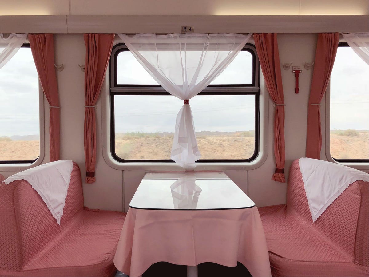 A table in a train car. The upholstery and curtains are different shades of pink.