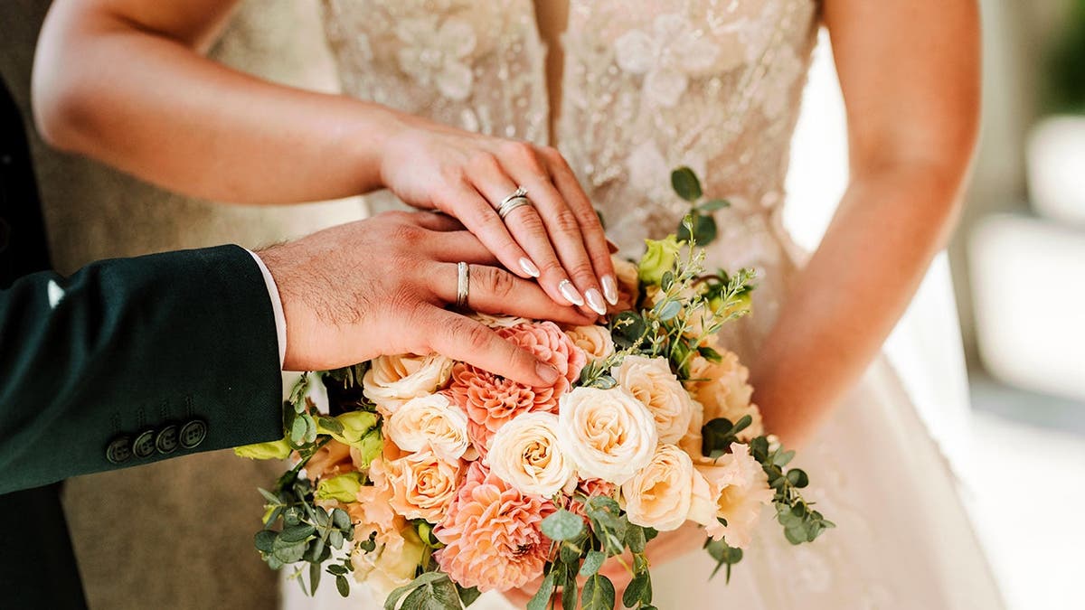 A bride and groom hold hands around a bouquet