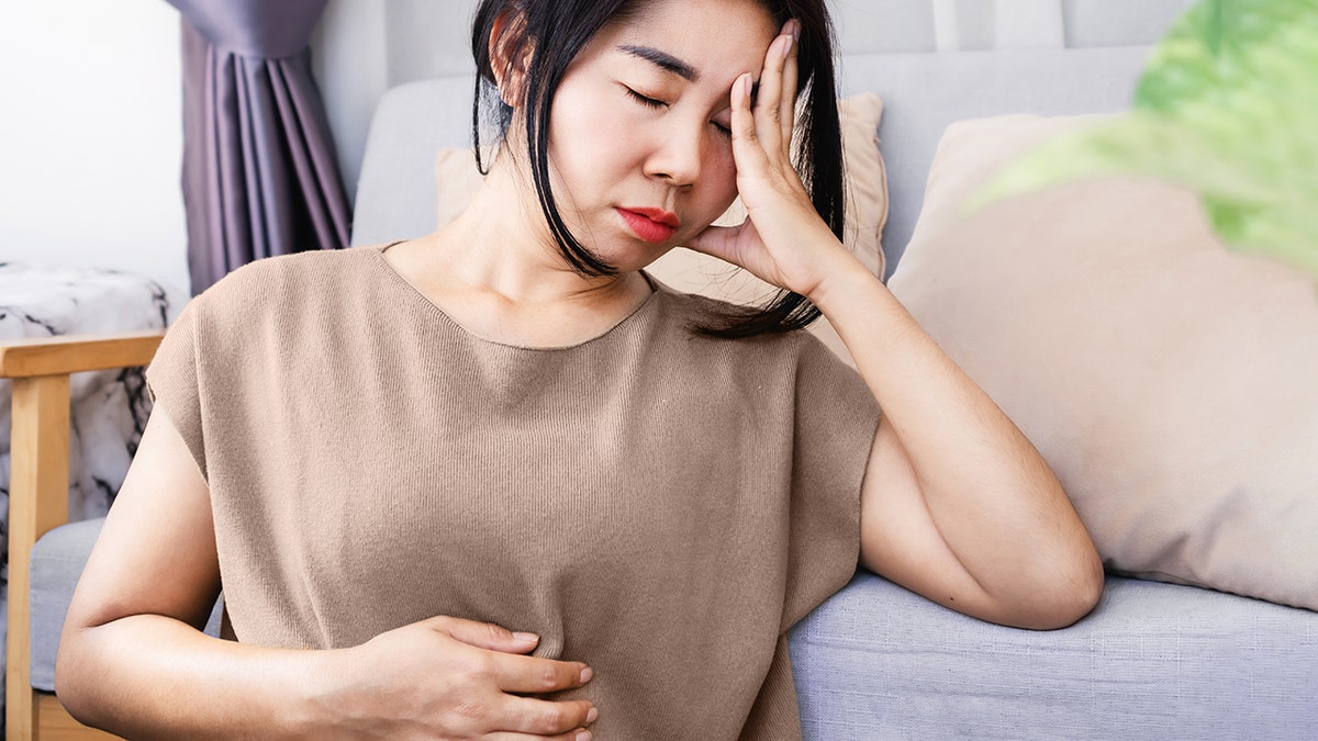 Woman holding head and stomach with eyes closed, signaling pain and gut-brain balance disruption.