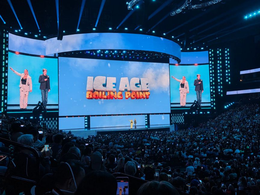 Two people stand on stage in front of a screen with the words "Ice Age Boiling Point" in front of a crowd of people.
