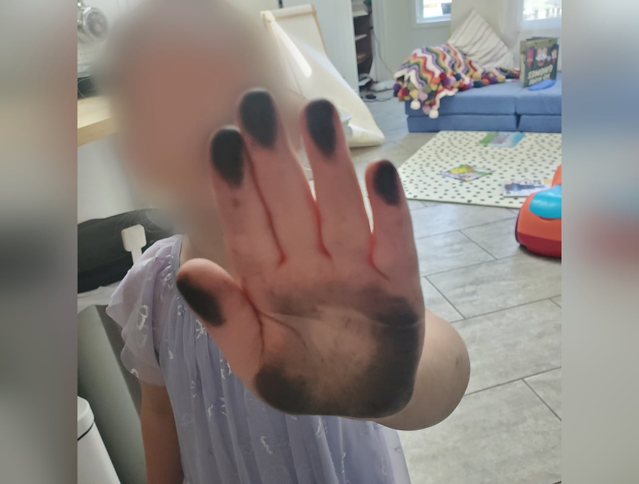 A young child holds up her hand for the camera. It has black grime on it.
