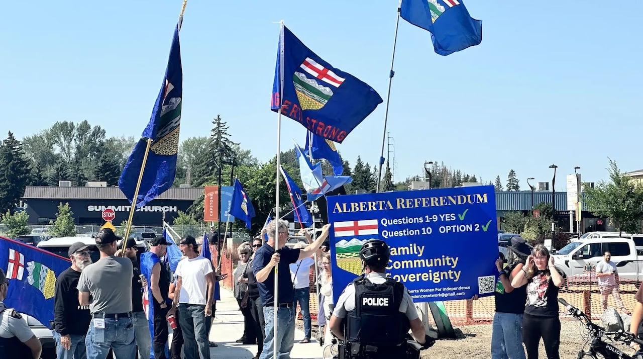A police man stands in front of people waving alberta independance flags.