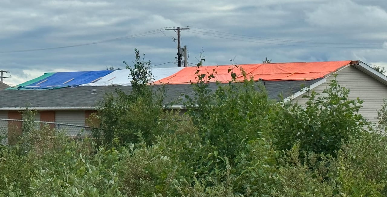A building has blue, grey, green and organge tarps stretched across the roof.