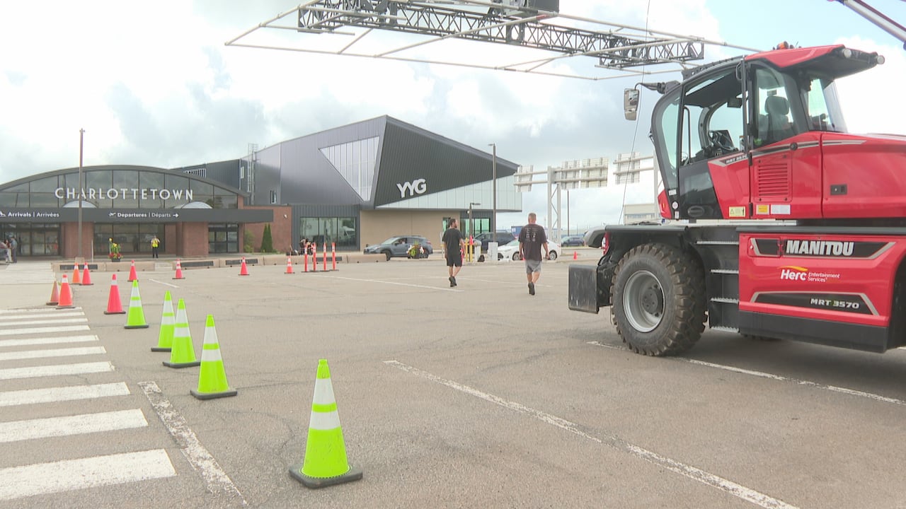 People walk near traffic cones and a large, red vehicle in front of a large building.