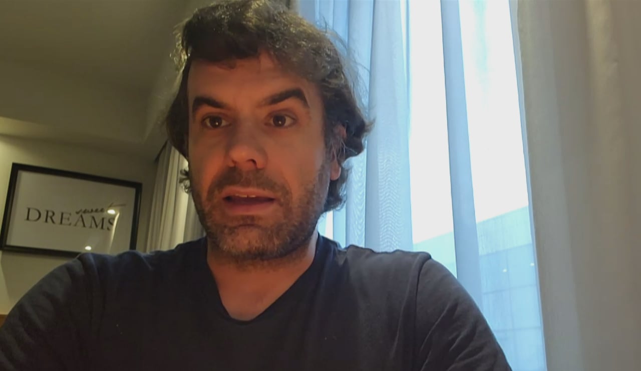 A man with curly dark hair is seen speaking.