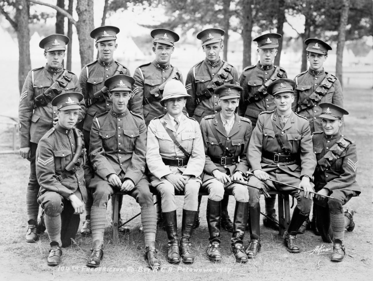 A black and white photo of 12 soldiers sitting in two rows in uniforms with one man, Walter Blair, sitting front and centre in a whiter uniform with a pith helmet on.