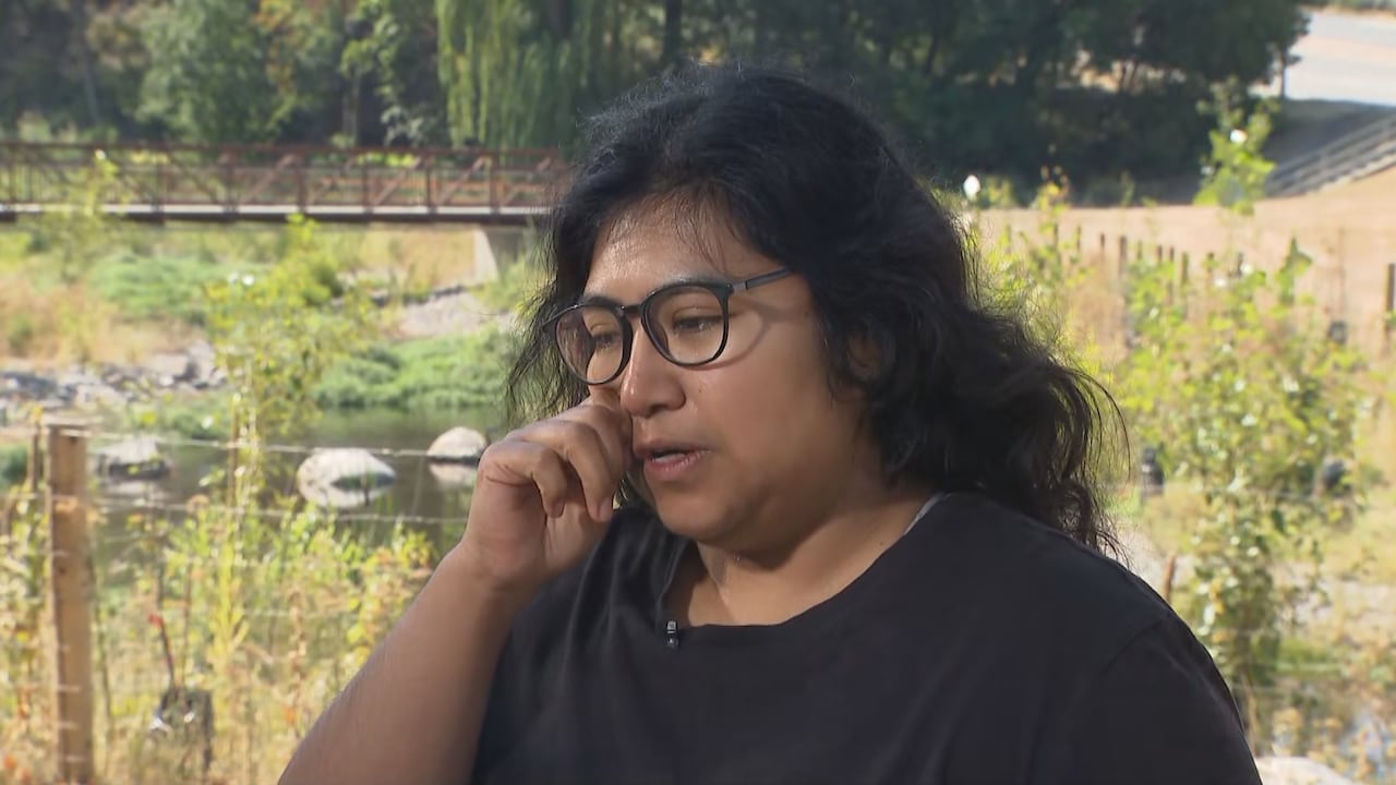 A woman wipes away tears while standing in front of a park environment.