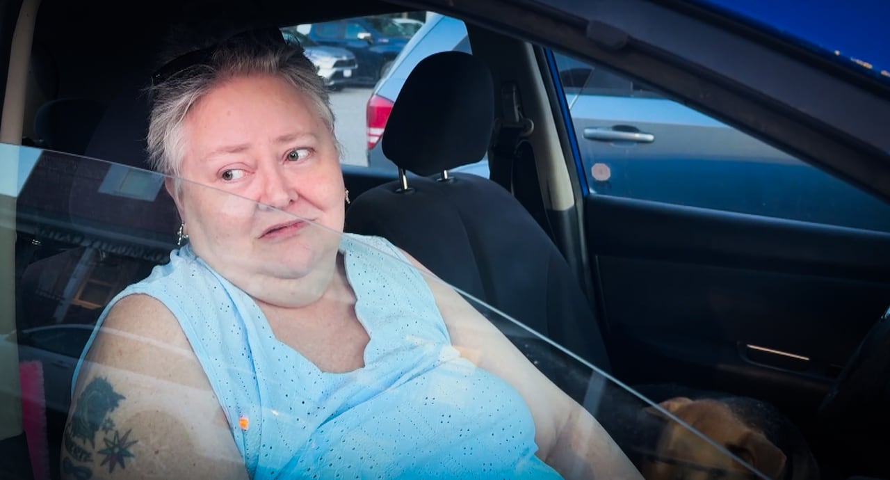 A woman in a car looks off into the distance.