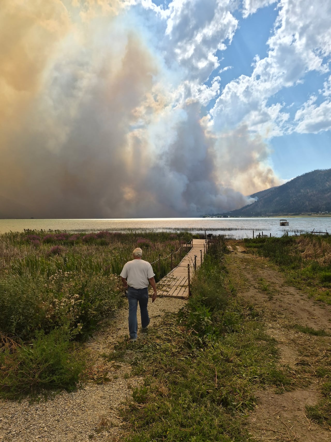 A man walks towards the water with smoky skies in the background.