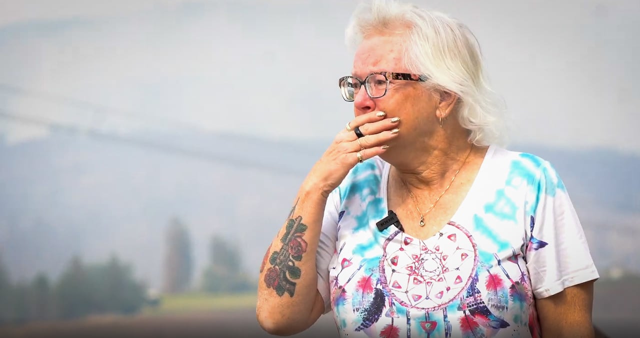 A woman looks off into the distance with smoke in the background.