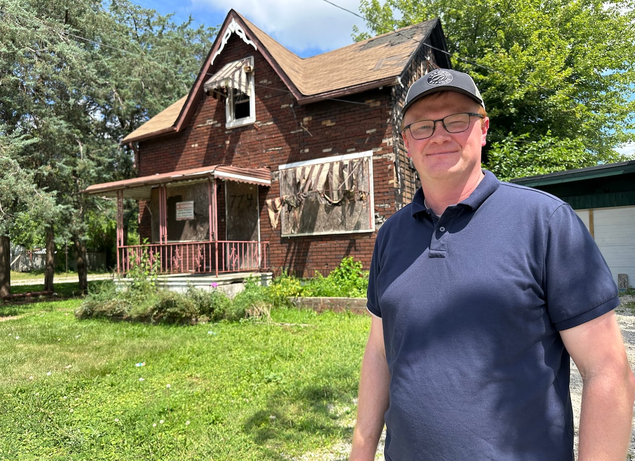A man standing in front of a boarded up home.