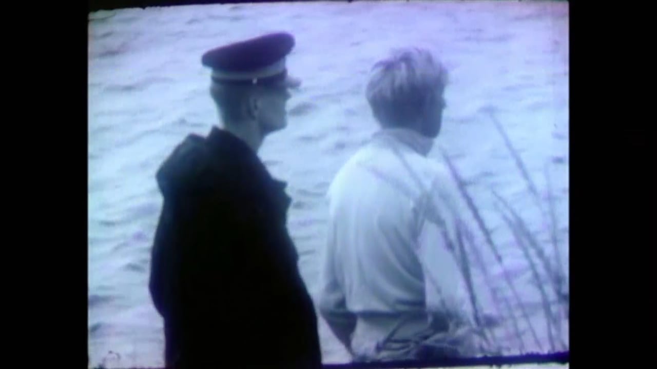 A black and white image shows a young man with an RCMP officer beside the ocean.