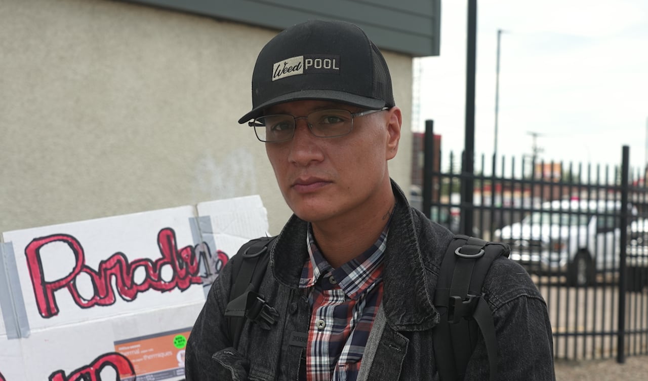 A man in a black cap and jacket stares directly at the camera.