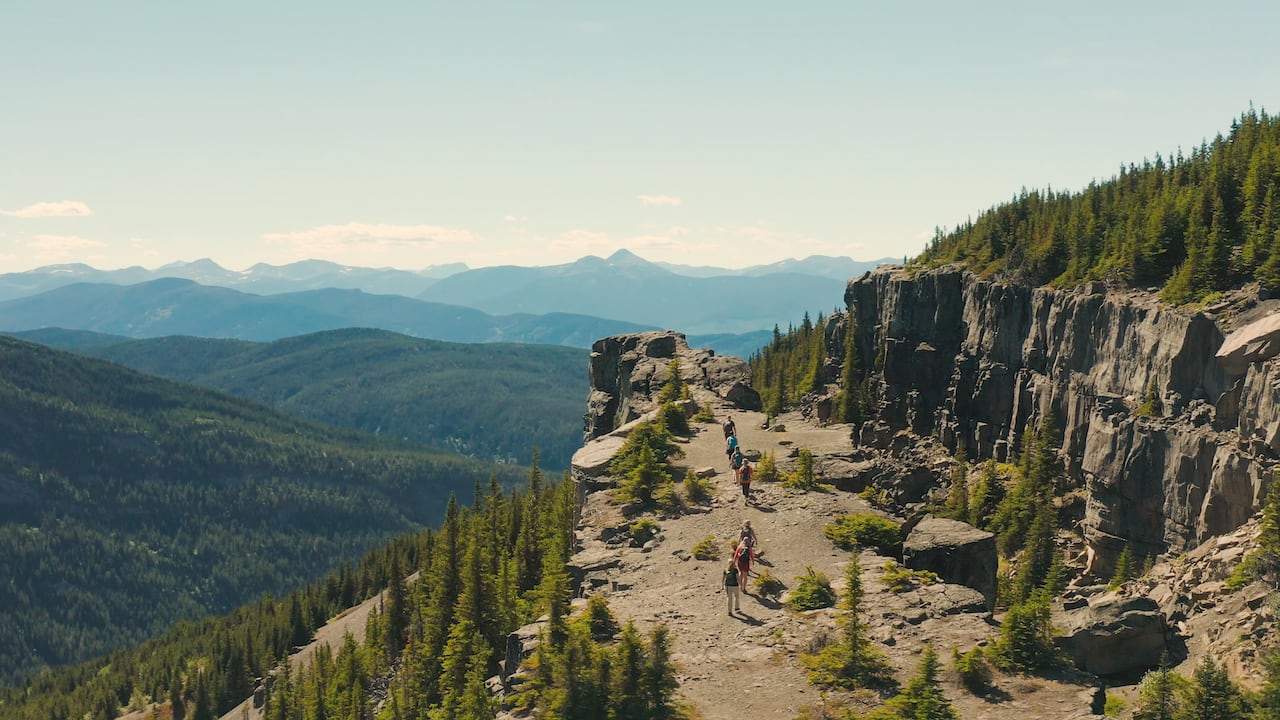 A group of hikers traversing a mountain trail surrounded by rocky terrain and lush greenery with scenic views of peaks and valleys in the distance.