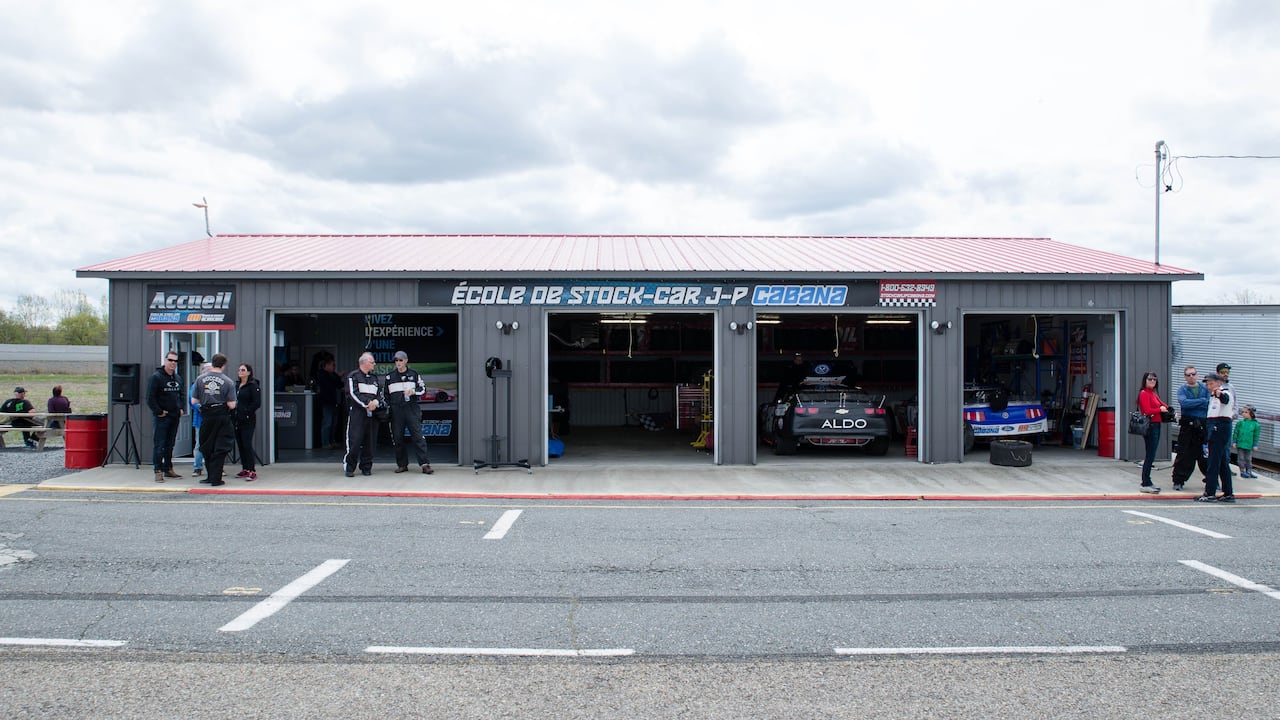 People at a racetrack stand outside a garage structure.