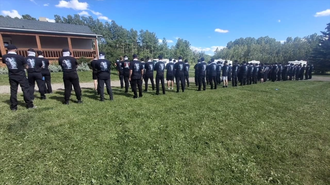 Men stand in ranks outside a building.